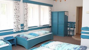 Una habitación con una cama curvada, un escritorio y una silla. Hay dos ventanas con cortinas, un armario y una araña.