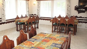 Un comedor con una larga mesa y múltiples sillas, ventanas amplias con cortinas y una araña.