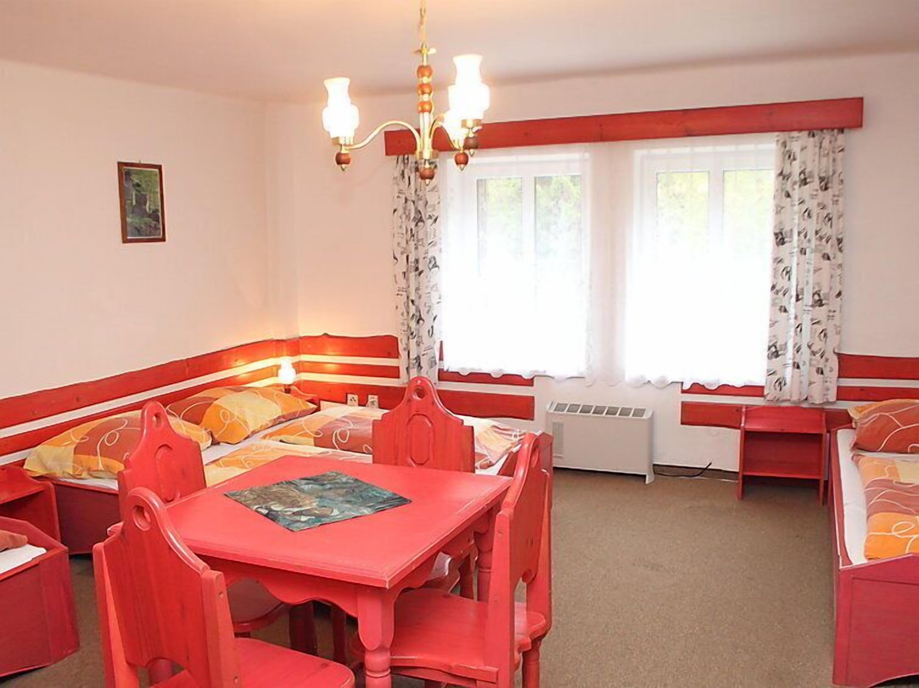 Ein Zimmer in Rot und Weiß gehalten, mit einem Bett, einem Kopfteil, einem Esstisch mit Stühlen und einer Deckenleuchte.
