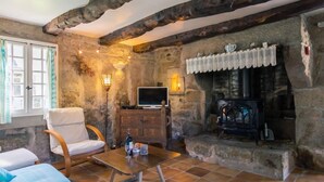 Ein rustikaler Raum mit Kamin aus Stein, einem Fernseher und einer gemütlichen Sitzecke mit Sessel und Sofa.