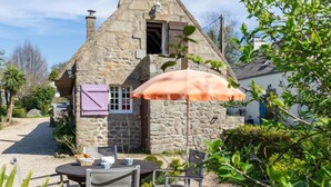 Ein Steinhäuschen mit einer kleinen Terrasse, einem Tisch mit Stühlen und einem Sonnenschirm.