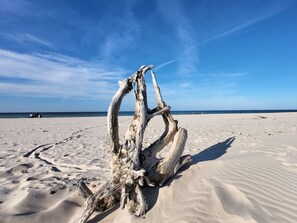 Una estructura de madera a la deriva en una playa arenosa con un cielo azul despejado.