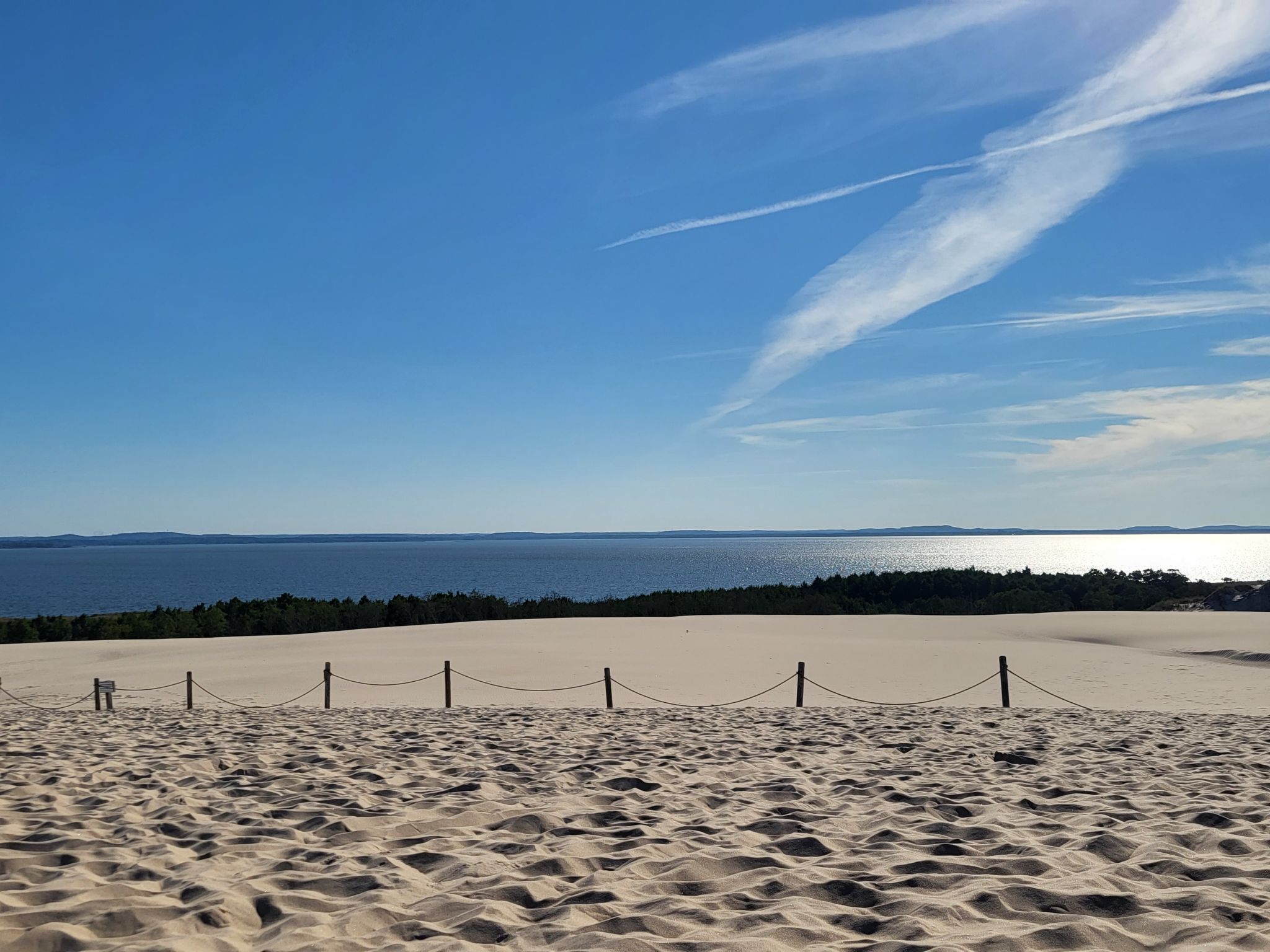 Ein Strand mit Zaun und freiem Blick auf das Meer und das entfernte Land.