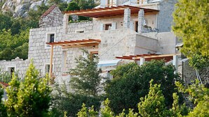 A multi-story stone building with balconies, set against a mountainous backdrop.