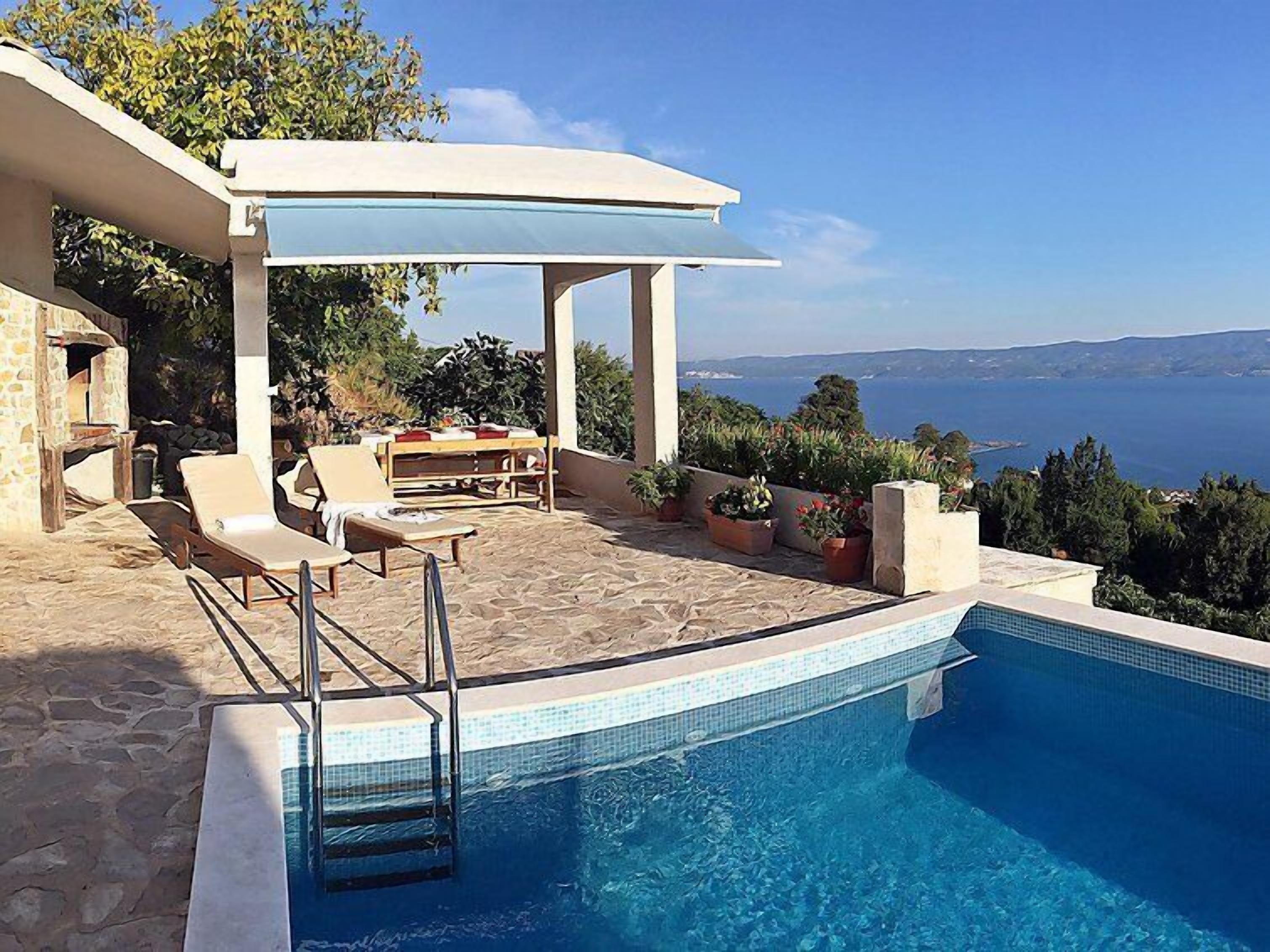 A poolside area with lounge chairs, a barbecue setup, and a view of the sea.