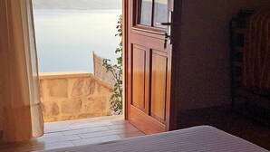 A room with a wooden door leading to a balcony overlooking a calm body of water and distant hills.