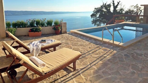 A poolside area with lounge chairs, a small table with a book, and a view of the sea.