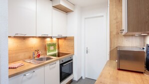 Una cucina compatta con mobili bianchi, un piano di lavoro in legno, un lavello in acciaio inossidabile, un forno a incasso e un piccolo frigorifero.