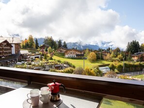 Un complejo turístico de montaña con edificios de estilo chalet, un comedor con mesa y juego de café, y vistas del paisaje circundante.