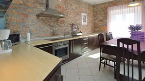 A kitchen with a stone wall, a dining area with a table and chairs, and a hanging light fixture. - Vacation home Marija by Interhome (Oklaj)