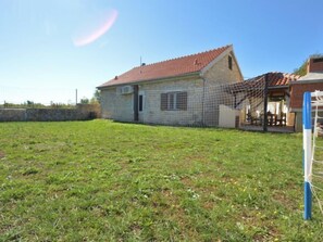 A single-story house with a tiled roof, a fenced yard, and a clear sky.