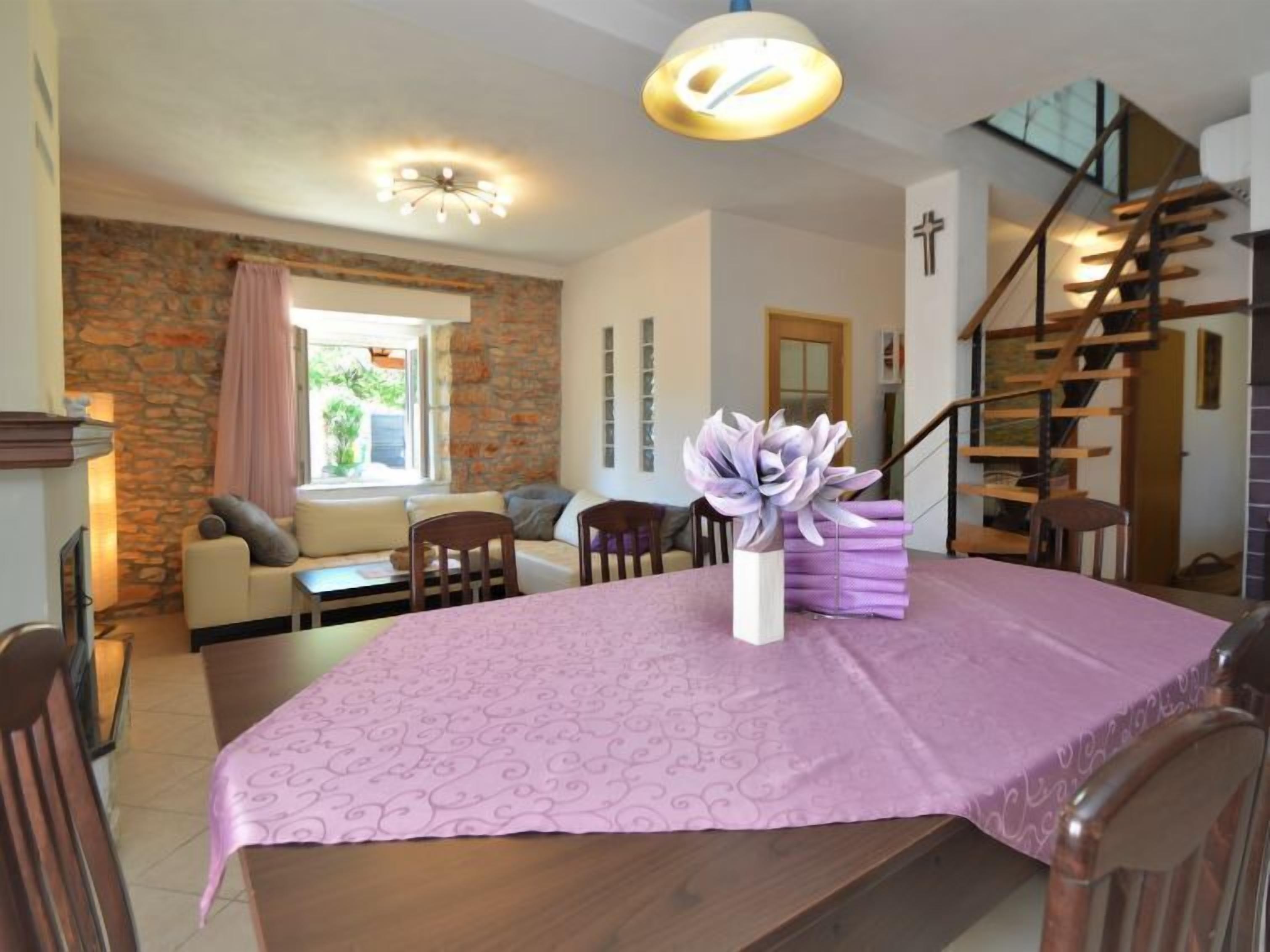 Un coin repas avec une table dressée pour quatre personnes, un vase rempli de fleurs, un escalier et un mur en pierre.