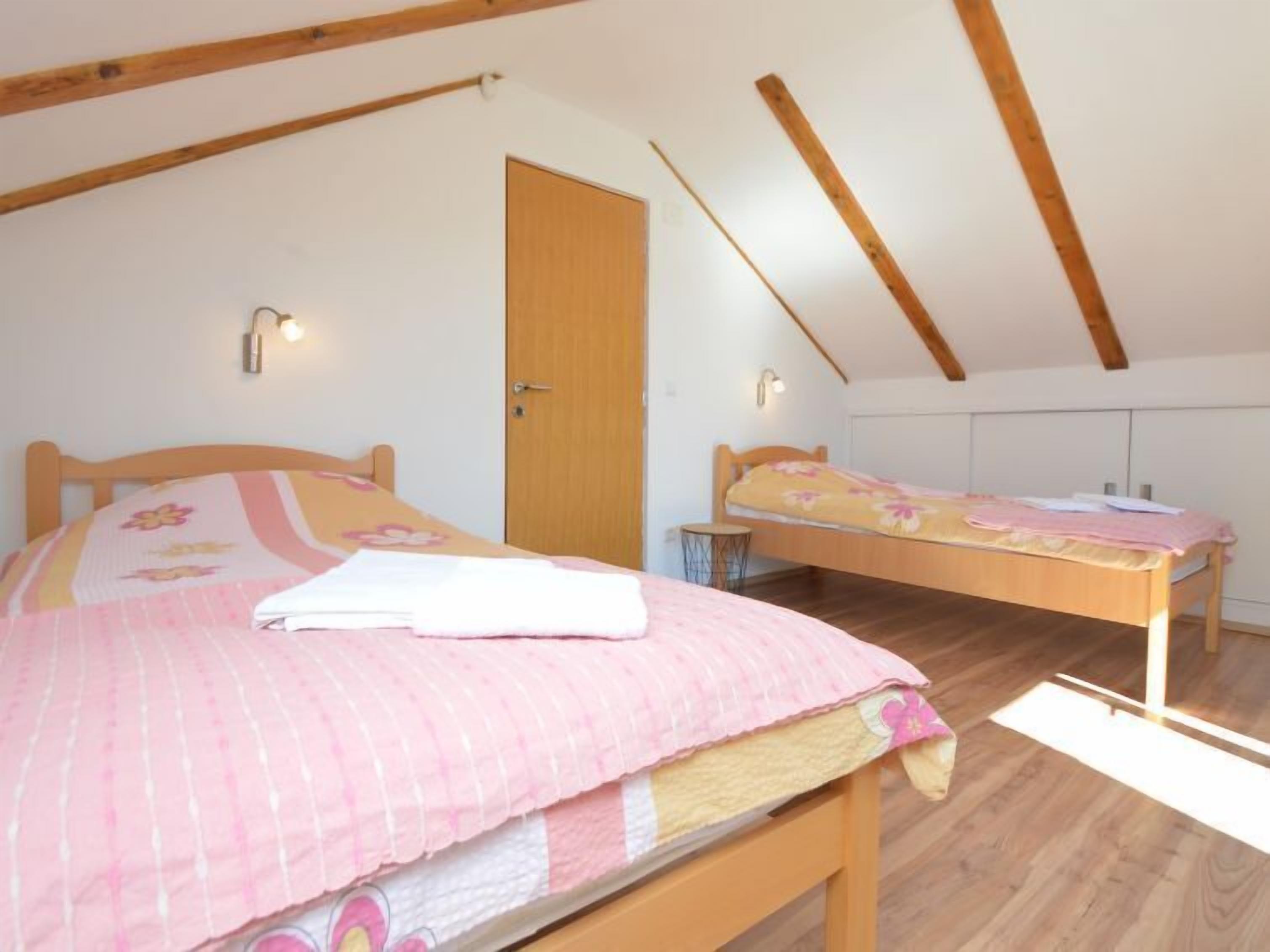 A bedroom with a wooden bed, a smaller bed, a door, and a sloped ceiling.