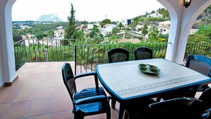 Un balcón con mesa y sillas, con vistas a una colina con edificios y árboles.
