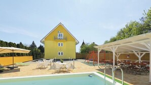 Ein gelbes Gebäude mit Schwimmbad, Außenbereich mit Sitzgelegenheiten und überdachter Terrasse.