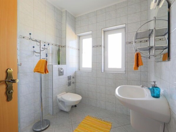 A bathroom with a toilet, sink, and shower. There are towels hanging on hooks and a window providing natural light.
