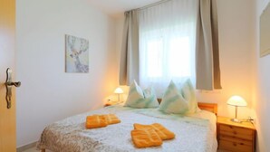 Ein Schlafzimmer mit einem Bett, zwei Nachttischen, einem Fenster mit Vorhängen und einer Wandlampe.