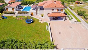 Ein großes Haus mit Swimmingpool, Trampolin und gepflegtem Rasen.