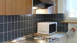 Una cocina con microondas, pileta de acero inoxidable y salpicadero de azulejos negros.