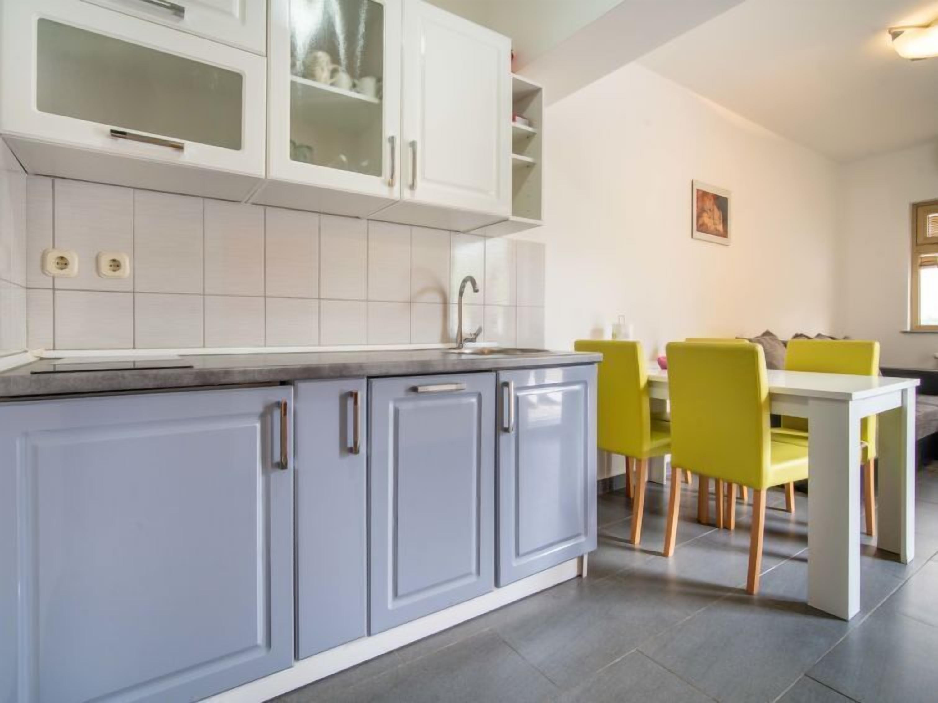 Una cocina moderna con armarios grises, una encimera blanca y un área de comedor con sillas amarillas y una mesa blanca.