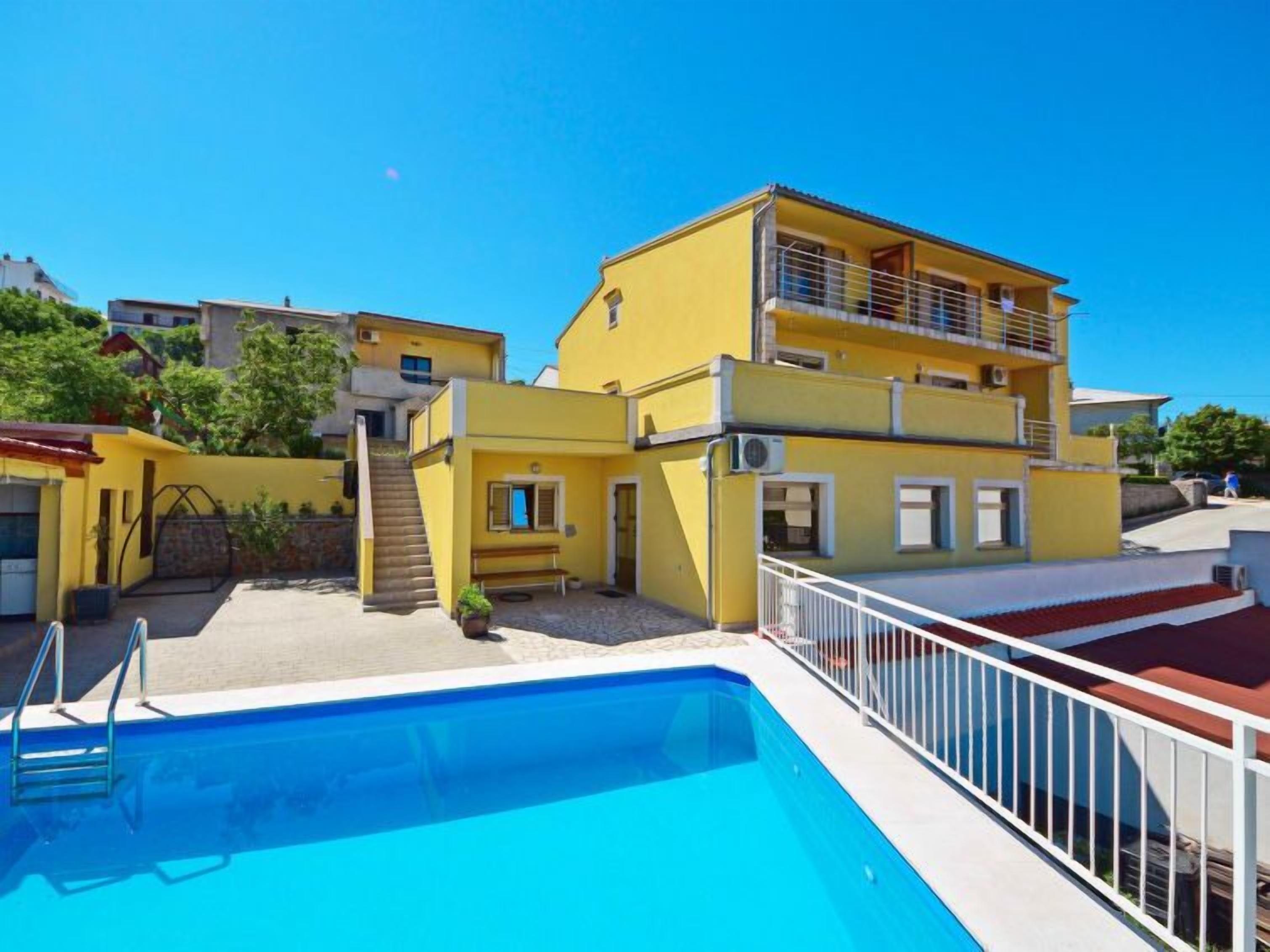 A yellow building with a pool, a staircase, and a balcony.
