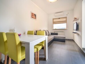 Un salon moderne avec une table blanche et des chaises jaunes, un canapé gris et un téléviseur posé sur une étagère.