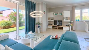 Una sala de estar moderna con una mesa de centro de vidrio, un sofá, un televisor y un comedor con un armario blanco.