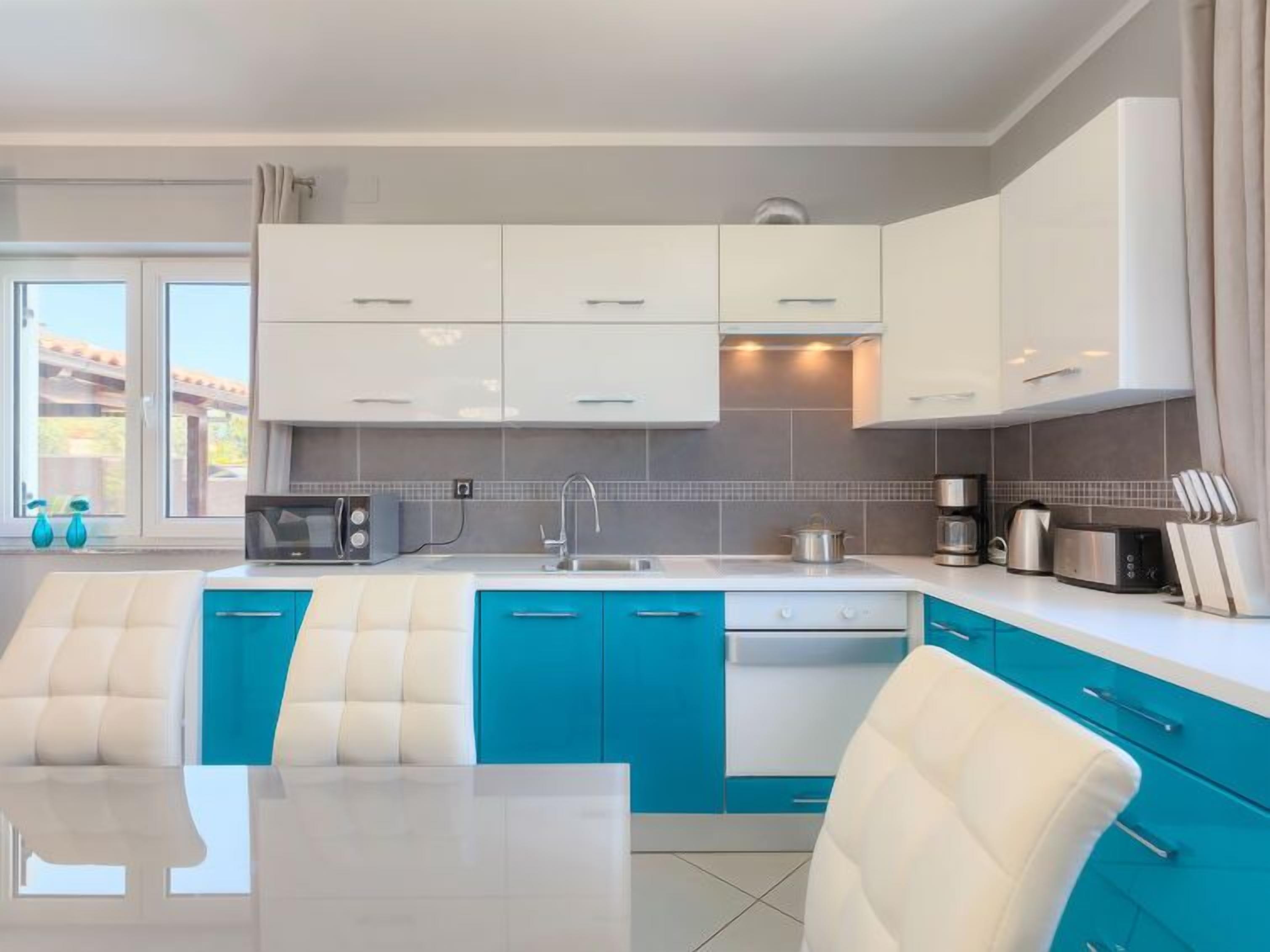 A modern kitchen with white and blue cabinetry, a microwave, a kettle, and a coffee maker.