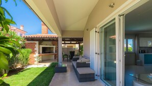 Un patio moderno con una parrilla, mobiliario exterior y una puerta de cristal que da a una cocina.