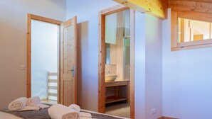 Una stanza con un letto, una panca di legno e un bagno visibile attraverso una porta aperta.