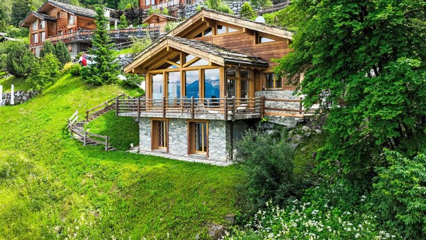 Un chalet in legno con fondamenta in pietra, un balcone e vista sulle montagne.