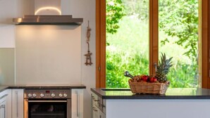Una cucina moderna con forno in acciaio inossidabile, una porta in legno che si affaccia sul verde e un cesto di frutta sul piano di lavoro.