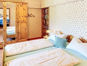 Ein Schlafzimmer mit einem Bett, einem Holzschrank, einem Bücherregal und Wandtapete mit Muster.