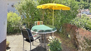 Une terrasse avec une table et une chaise, un parasol jaune et une vue sur une zone boisée.