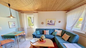Un salon avec un canapé bleu, une table basse en bois, une table à manger avec des chaises et une fenêtre avec des rideaux.