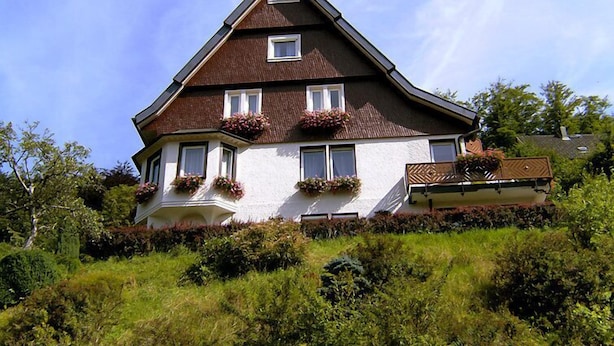 Une maison à deux étages, dotée d’un toit à forte pente, de lucarnes et de jardinières au deuxième étage.