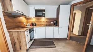 Ett kompakt kök med vita skåp, en inbyggd ugn, en mikrovågsugn och en kaffebryggare.
