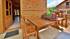 Eine Holzhütte mit Holztisch und -stühlen, einem Balkon mit Blumen und Blick ins Grüne.