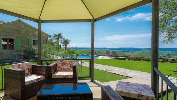 Ein überdachter Außenbereich mit Korbmöbeln und Blick auf einen Swimmingpool und die Landschaft.