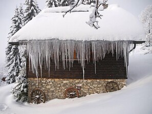 Une cabane en bois, avec des glaçons pendants du toit, entourée d’arbres couverts de neige.