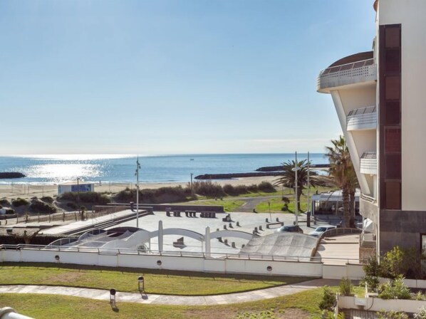 A coastal view with a modern building, a beach, and a skate park.