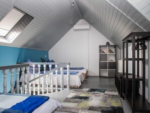 A bedroom with a sloped ceiling, a skylight, a staircase, a bed, a bookshelf, and a desk.