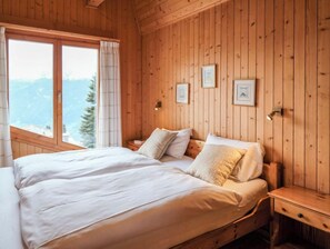 Une chambre à coucher aux murs lambrissés, avec un grand lit, deux tables de chevet et des tableaux encadrés accrochés au mur.