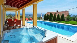 Une piscine avec un jacuzzi, un espace extérieur aménagé et une vue sur les maisons et les montagnes.