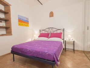 Un dormitorio con una cama, dos mesitas de noche, un estante en la pared y un cuadro.
