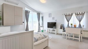 Ein modernes, helles Wohnzimmer mit Sofa, Fernseher, Esstisch und Küchenbereich.