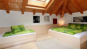 A bedroom with a sloped wooden ceiling, two beds with green bedding, a skylight, and artwork on the walls. - Frischmann by Interhome (Umhausen)