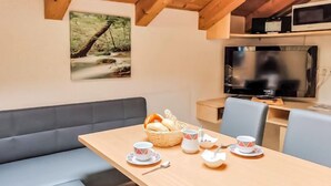 A cozy room with a wooden table set for tea, a sofa, and a TV on the wall. - Frischmann by Interhome (Umhausen)