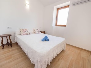 Un dormitorio con cama, una mesita de noche de madera, una ventana y un equipo de aire acondicionado.