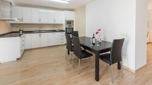 Een moderne keuken met witte kasten, een zwart aanrechtblad en een eethoek met een donkere tafel en zwarte stoelen.
